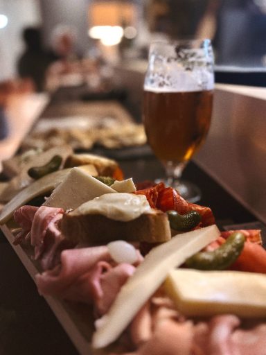 Pl plateau garni de charcuterie, fromages et légumes, avec une bière à l'arrière-plan.