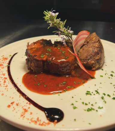 Plat de viande avec sauce rouge, garniture de purée et de légumes, décoré d'herbes.